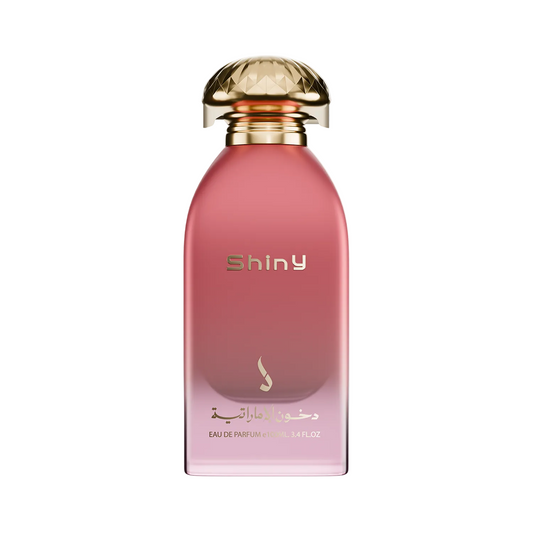 Shiny Eau de Parfum bottle in a soft pink glass with a metallic gold cap, shown on a plain white background.